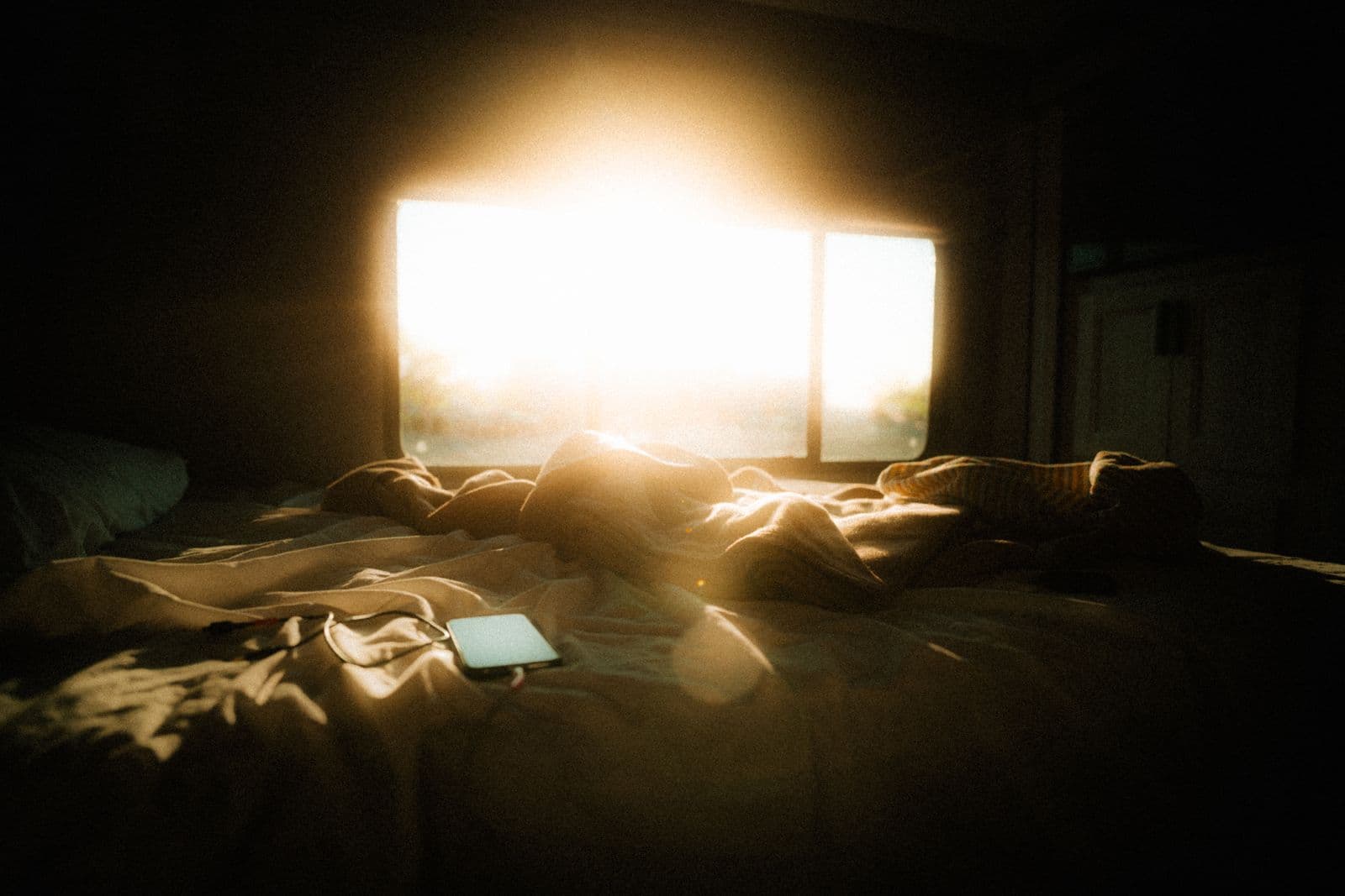 Morning light falling across an unmade bed with a phone nearby